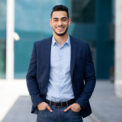 Handsome middle-eastern guy young businessman in stylish suit posing next to office center, smiling arab entrepreneur having break after successful busienss meeting, standing on street, copy space